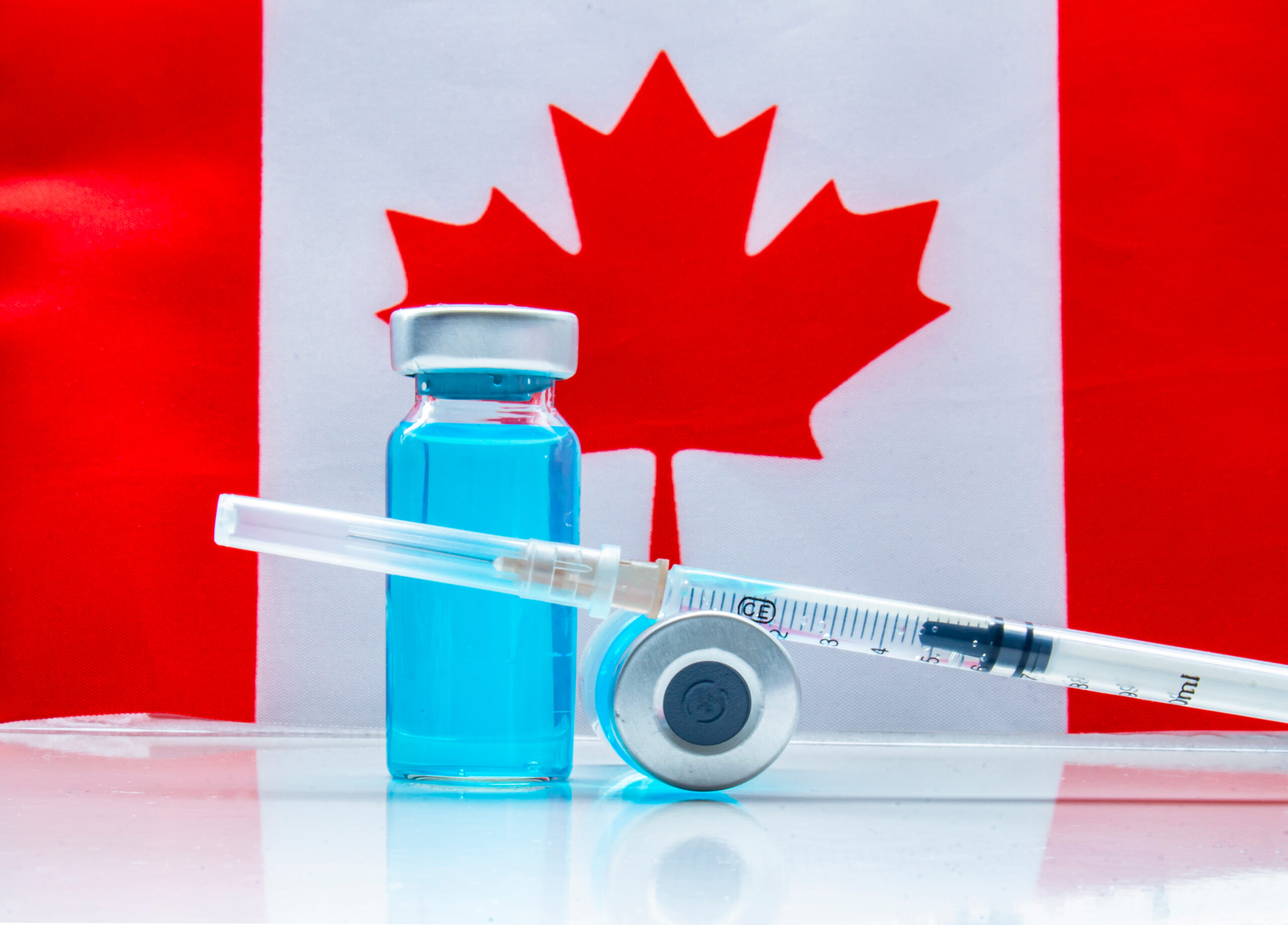 Vaccine on a vial bottle and injection Syringe with a Canadian flag on the background
