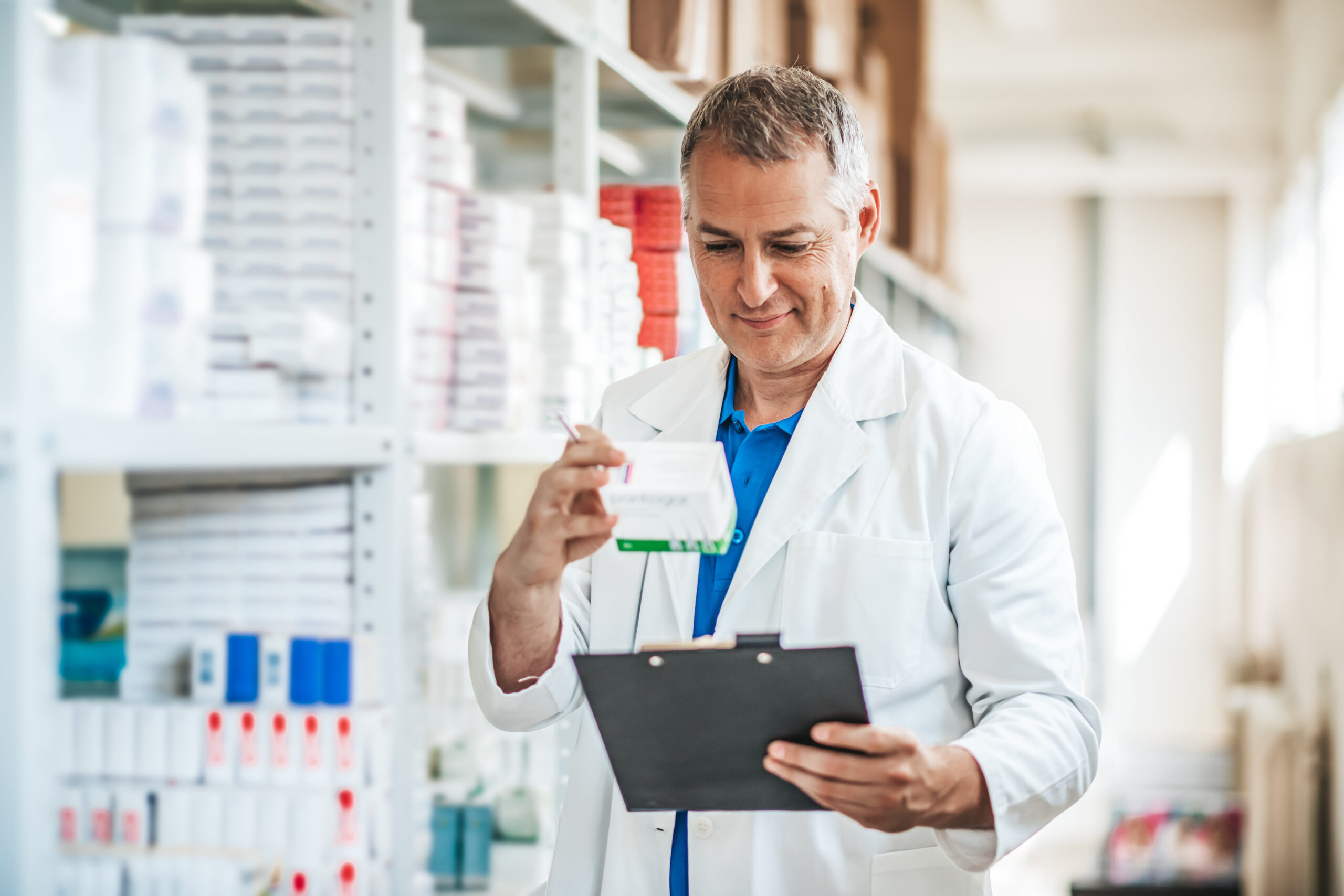 Cheerful pharmacist chemist man standing in pharmacy drugstore. Pharmacist man in the warehouse holding boxes with drugs in hands. Healthcare business. Medicine and pharmacy